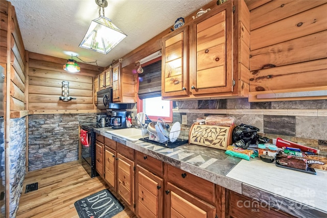 kitchen featuring rustic walls, sink, hanging light fixtures, light hardwood / wood-style floors, and a textured ceiling