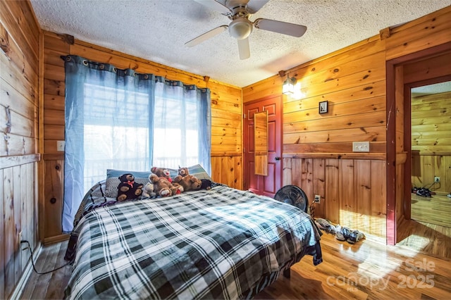 bedroom with hardwood / wood-style flooring, ceiling fan, a textured ceiling, and wooden walls