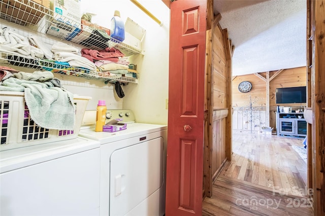 laundry room with washer and dryer, a textured ceiling, light hardwood / wood-style flooring, and wood walls