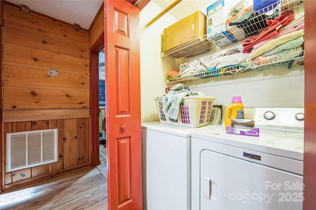 clothes washing area featuring washer and dryer, light wood-type flooring, a textured ceiling, and wooden walls