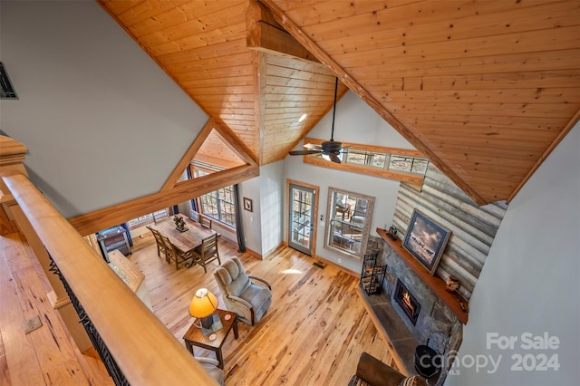 living room with ceiling fan, a stone fireplace, light hardwood / wood-style flooring, high vaulted ceiling, and wood ceiling