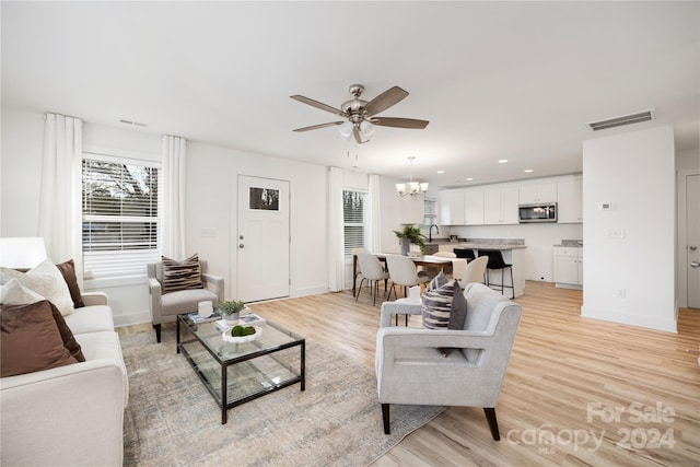 living room with ceiling fan with notable chandelier and light hardwood / wood-style flooring