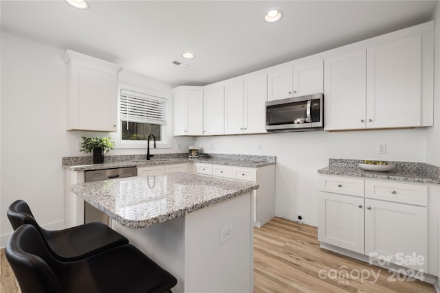 kitchen with light wood-type flooring, stainless steel appliances, sink, white cabinets, and a kitchen island