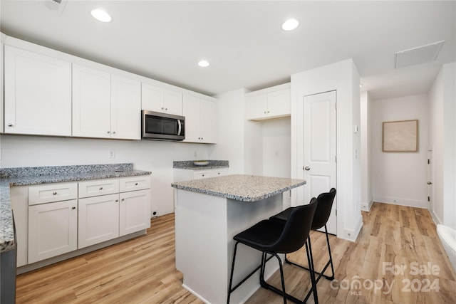 kitchen with a breakfast bar, a center island, light hardwood / wood-style flooring, light stone countertops, and white cabinetry