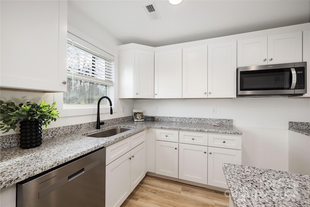 kitchen featuring white cabinetry, sink, light stone counters, appliances with stainless steel finishes, and light wood-type flooring