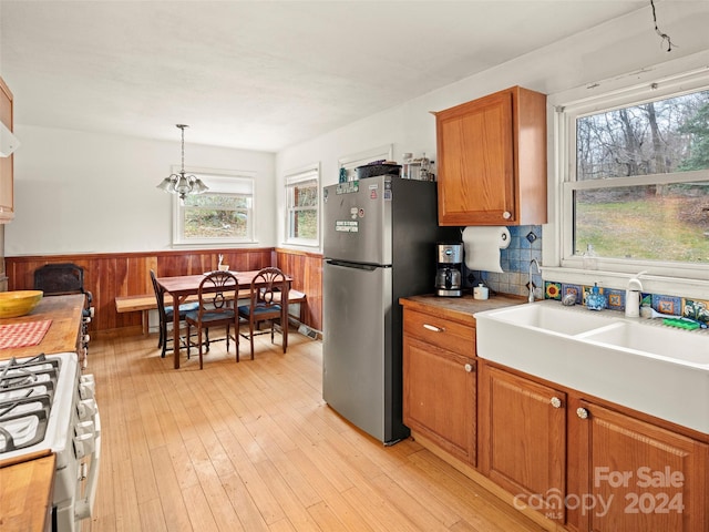 kitchen with stainless steel fridge, wooden walls, decorative light fixtures, light hardwood / wood-style flooring, and white gas stove