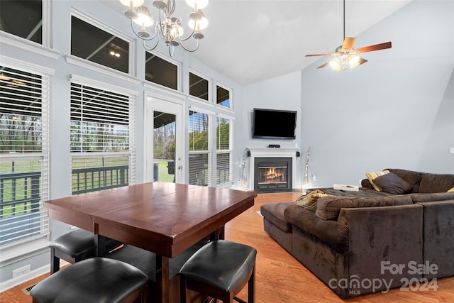 dining area with ceiling fan with notable chandelier, light hardwood / wood-style floors, high vaulted ceiling, and a wealth of natural light