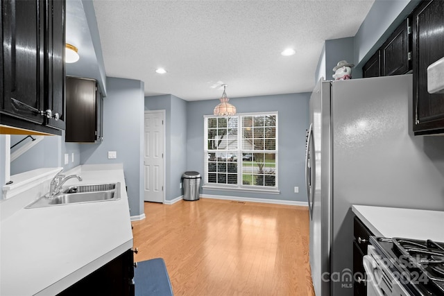 kitchen with pendant lighting, sink, a textured ceiling, appliances with stainless steel finishes, and light hardwood / wood-style floors