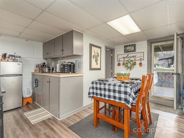 kitchen with gray cabinetry, a drop ceiling, stainless steel fridge, wood walls, and wood-type flooring