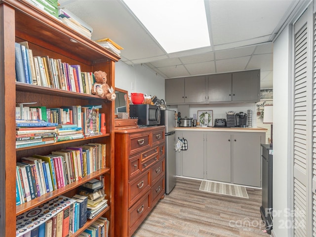 interior space with stainless steel refrigerator, a drop ceiling, and light wood-type flooring