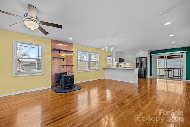 unfurnished living room with ceiling fan with notable chandelier, light wood-type flooring, and a wood stove