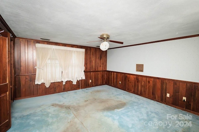 carpeted empty room featuring a textured ceiling, ceiling fan, ornamental molding, and wood walls