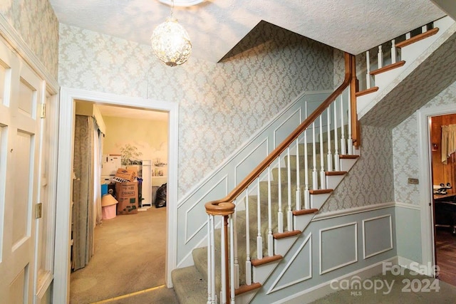 stairs featuring carpet flooring, a notable chandelier, and a textured ceiling