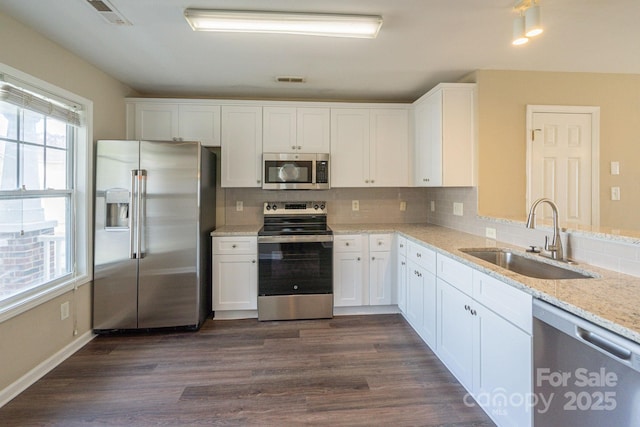 kitchen with appliances with stainless steel finishes, light stone counters, dark wood-type flooring, sink, and white cabinetry