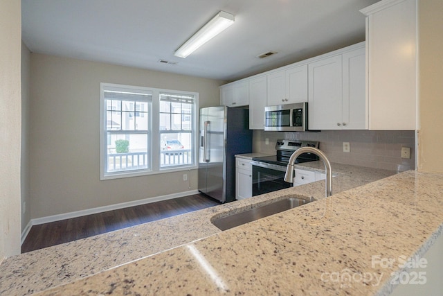 kitchen with light stone countertops, appliances with stainless steel finishes, backsplash, sink, and white cabinets