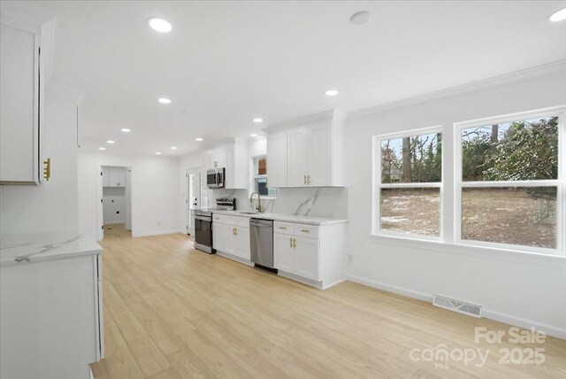 kitchen featuring appliances with stainless steel finishes, tasteful backsplash, white cabinetry, sink, and light stone countertops