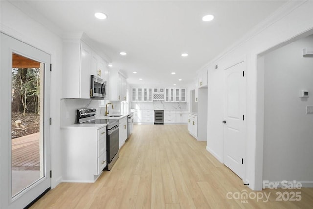 kitchen featuring tasteful backsplash, sink, white cabinets, stainless steel appliances, and light wood-type flooring