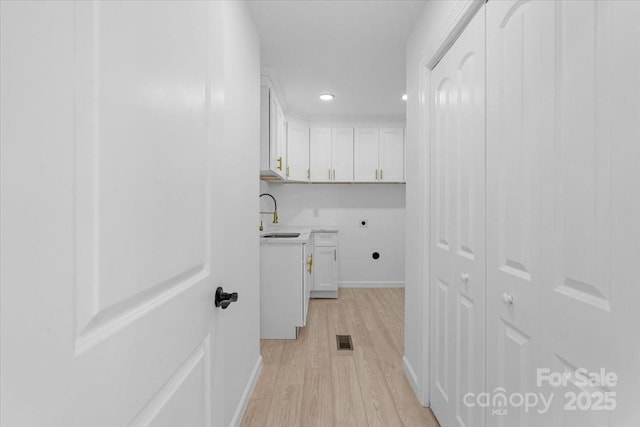 laundry area with electric dryer hookup, sink, light hardwood / wood-style floors, and cabinets