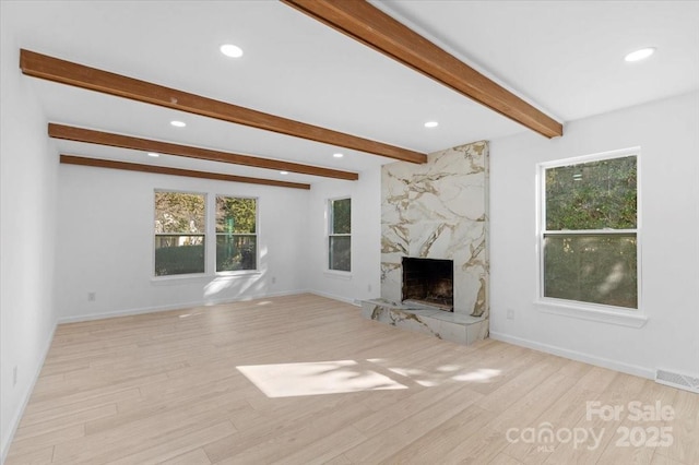 unfurnished living room with beamed ceiling, a high end fireplace, and light hardwood / wood-style flooring