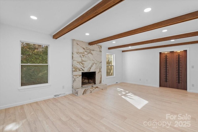 unfurnished living room with beam ceiling, light hardwood / wood-style flooring, and a premium fireplace