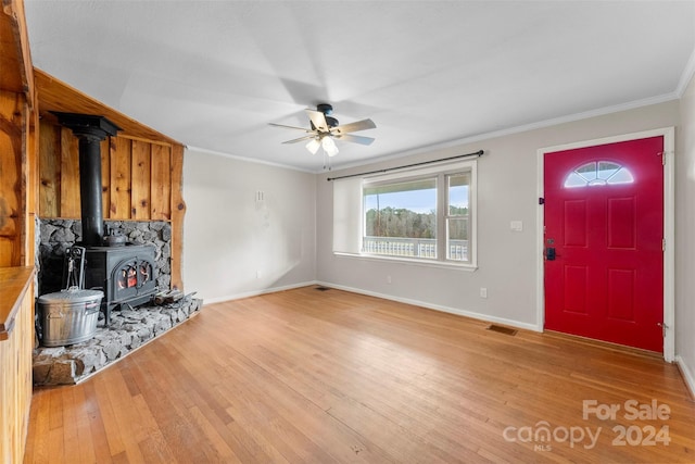 foyer entrance with wood-type flooring, a wood stove, ceiling fan, and crown molding