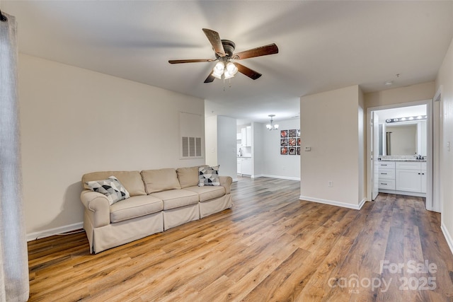 living room with ceiling fan with notable chandelier and light wood-type flooring