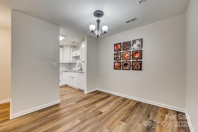 unfurnished dining area featuring sink, light hardwood / wood-style floors, and a notable chandelier