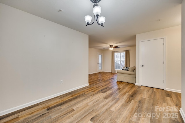 spare room with ceiling fan with notable chandelier and light wood-type flooring