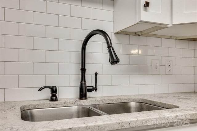 room details with white cabinets, decorative backsplash, light stone countertops, and sink