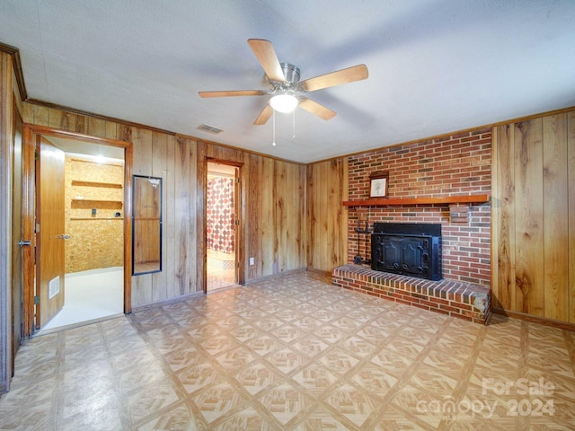 unfurnished living room with ceiling fan, wood walls, ornamental molding, and a fireplace