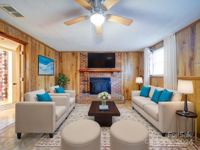 living room with ceiling fan, a brick fireplace, a textured ceiling, wooden walls, and light parquet flooring