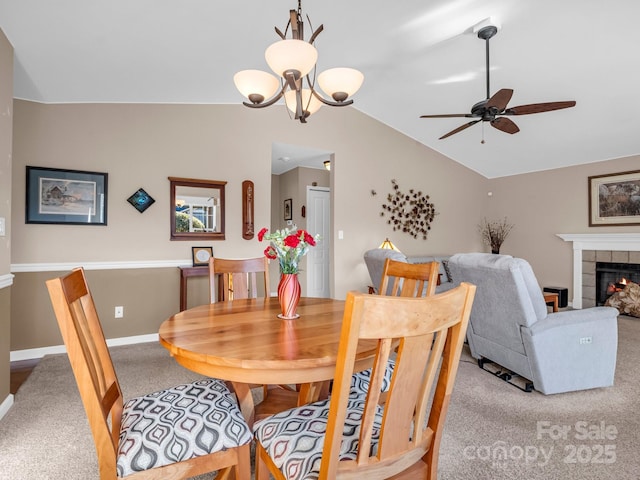 carpeted dining area with ceiling fan with notable chandelier, a fireplace, and vaulted ceiling