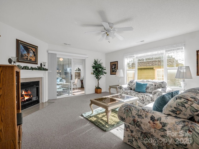 living room with light carpet, a textured ceiling, ceiling fan, and a tiled fireplace