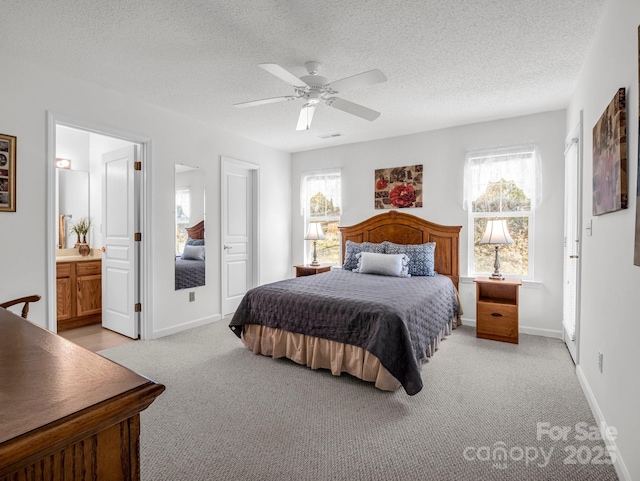 bedroom with ceiling fan, light colored carpet, a textured ceiling, and ensuite bath