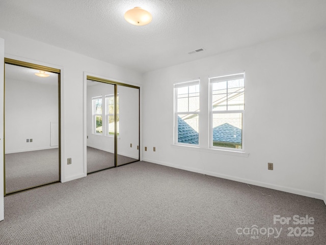 unfurnished bedroom featuring carpet, a textured ceiling, and multiple closets