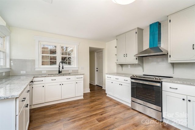 kitchen with wall chimney exhaust hood, sink, stainless steel electric range oven, hardwood / wood-style flooring, and white cabinets