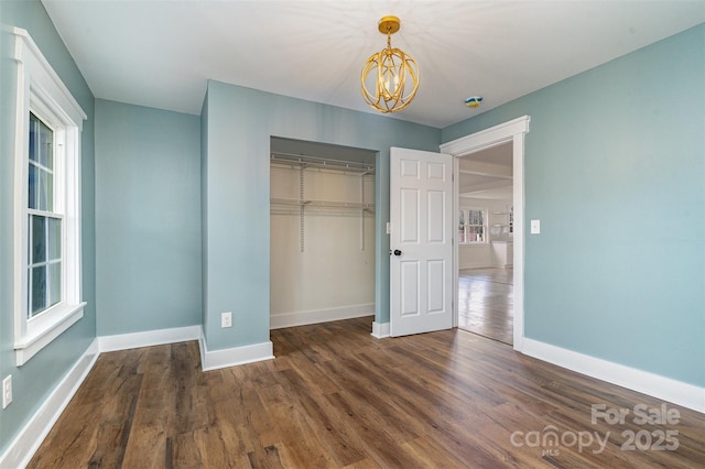 unfurnished bedroom featuring multiple windows, dark wood-type flooring, a chandelier, and a closet