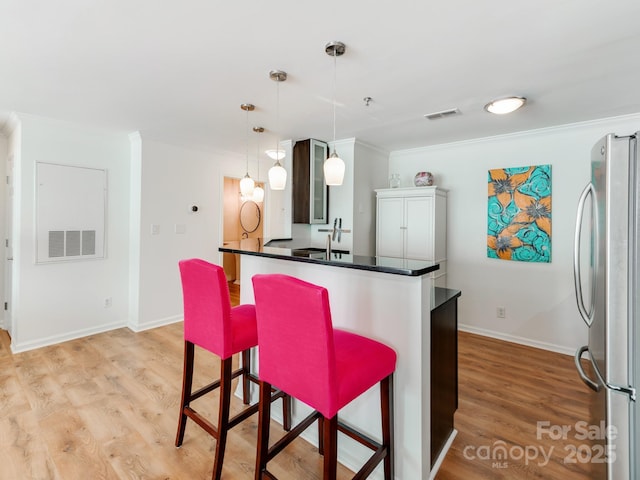 kitchen with ornamental molding, stainless steel fridge, a breakfast bar area, and pendant lighting