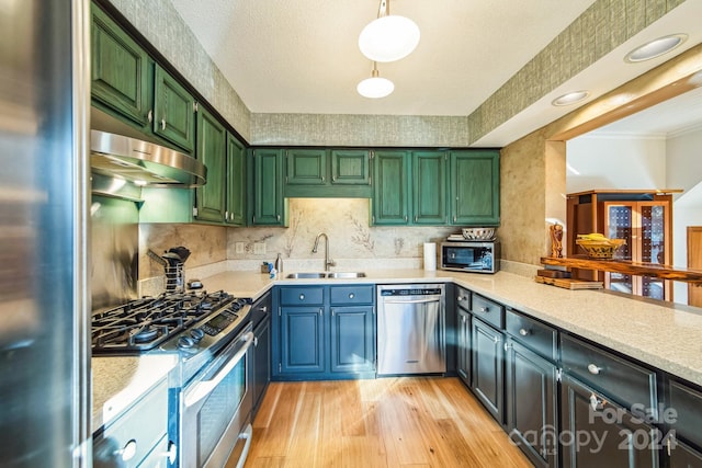 kitchen with sink, stainless steel appliances, decorative light fixtures, and light hardwood / wood-style floors