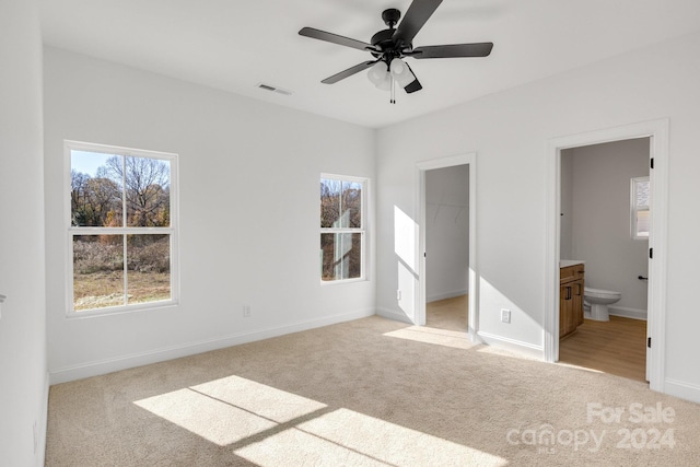 unfurnished bedroom with ensuite bath, a spacious closet, ceiling fan, light carpet, and a closet