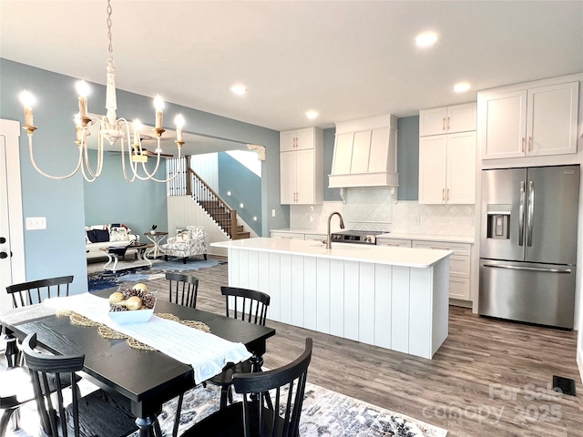 kitchen with white cabinetry, an inviting chandelier, premium range hood, a center island with sink, and appliances with stainless steel finishes