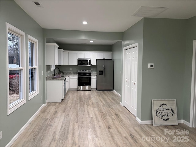 kitchen with white cabinets, sink, light hardwood / wood-style flooring, dark stone countertops, and stainless steel appliances