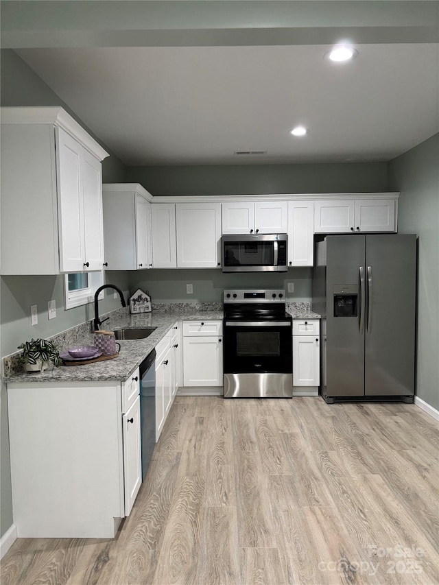 kitchen with sink, light hardwood / wood-style floors, light stone counters, white cabinetry, and stainless steel appliances