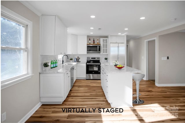 kitchen with a wealth of natural light, stainless steel appliances, a kitchen island, light stone counters, and white cabinets