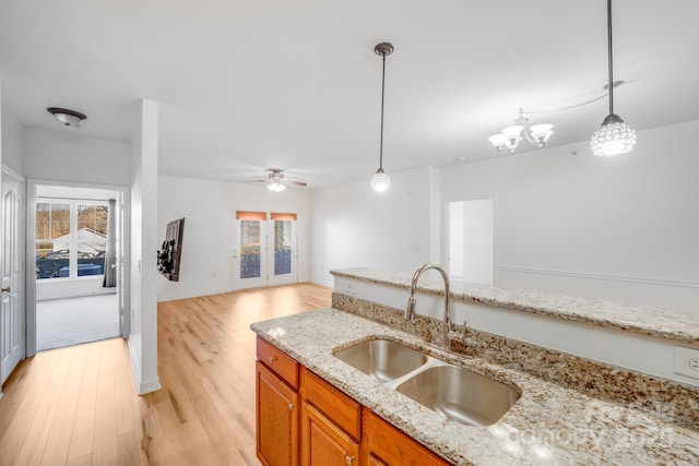 kitchen featuring light stone countertops, pendant lighting, ceiling fan with notable chandelier, and sink