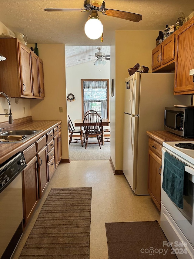 kitchen featuring lofted ceiling, white appliances, sink, ceiling fan, and a textured ceiling