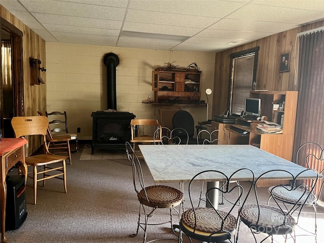 carpeted dining space featuring a paneled ceiling, a wood stove, and wooden walls