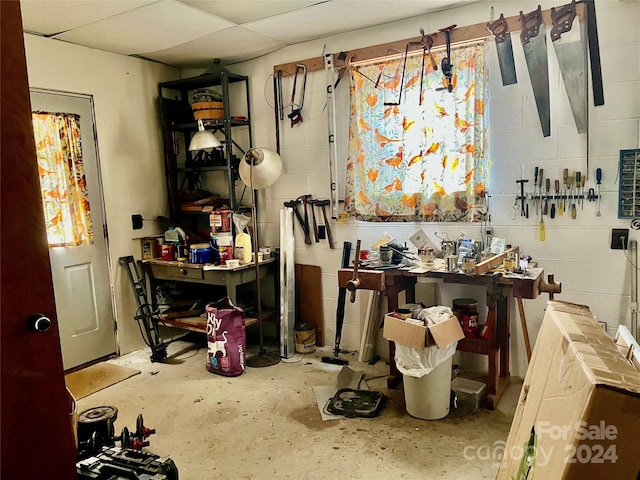 miscellaneous room featuring a workshop area, a paneled ceiling, and concrete floors