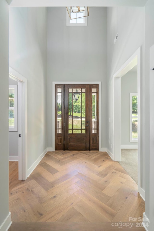 entryway featuring a towering ceiling, a healthy amount of sunlight, and light parquet flooring