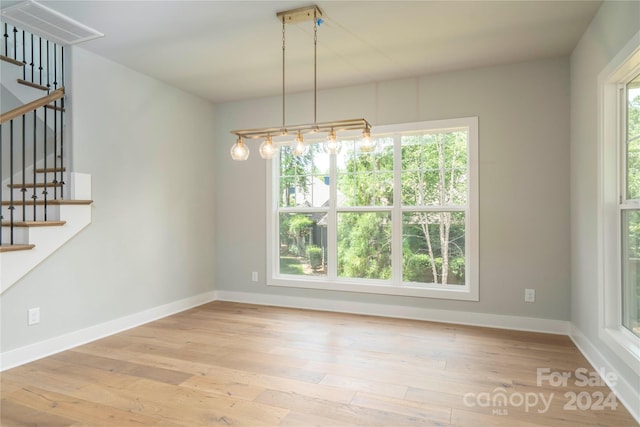 unfurnished dining area with light wood-type flooring, an inviting chandelier, and a wealth of natural light